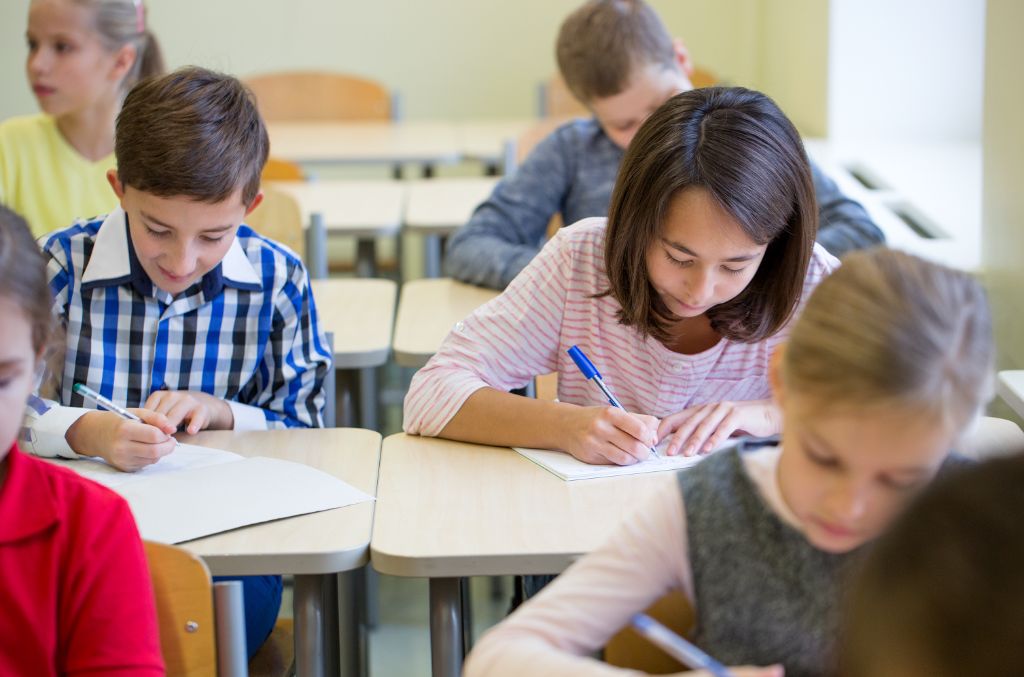Crianças sentadas em uma sala de aula realizam atividade escolar, representando um ambiente de educação em sala de aula. 